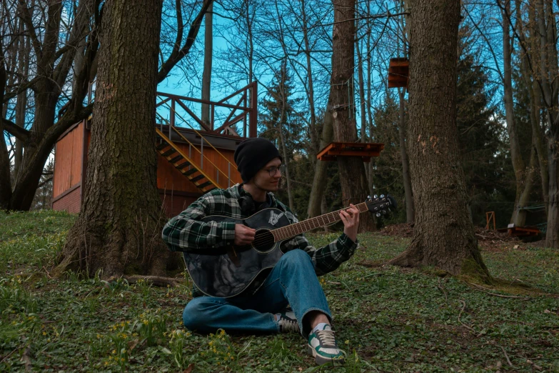 a man sits in the woods while holding a guitar