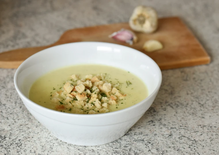 bowl of soup sitting on a counter with chopped vegetables and meat cubes