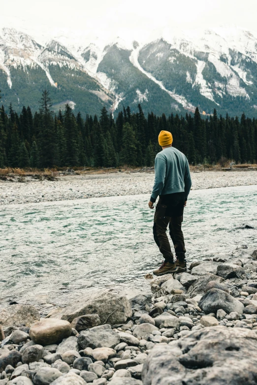 man standing on the edge of a river looking at the mountains