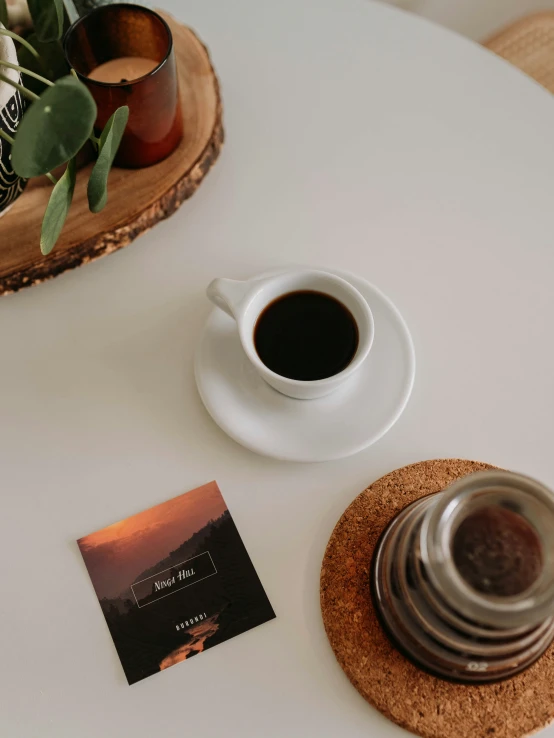 there is a cup of coffee, a plant and a book on the table