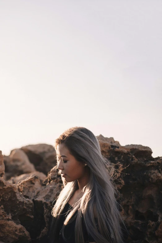 a young woman sitting near rocks and some water