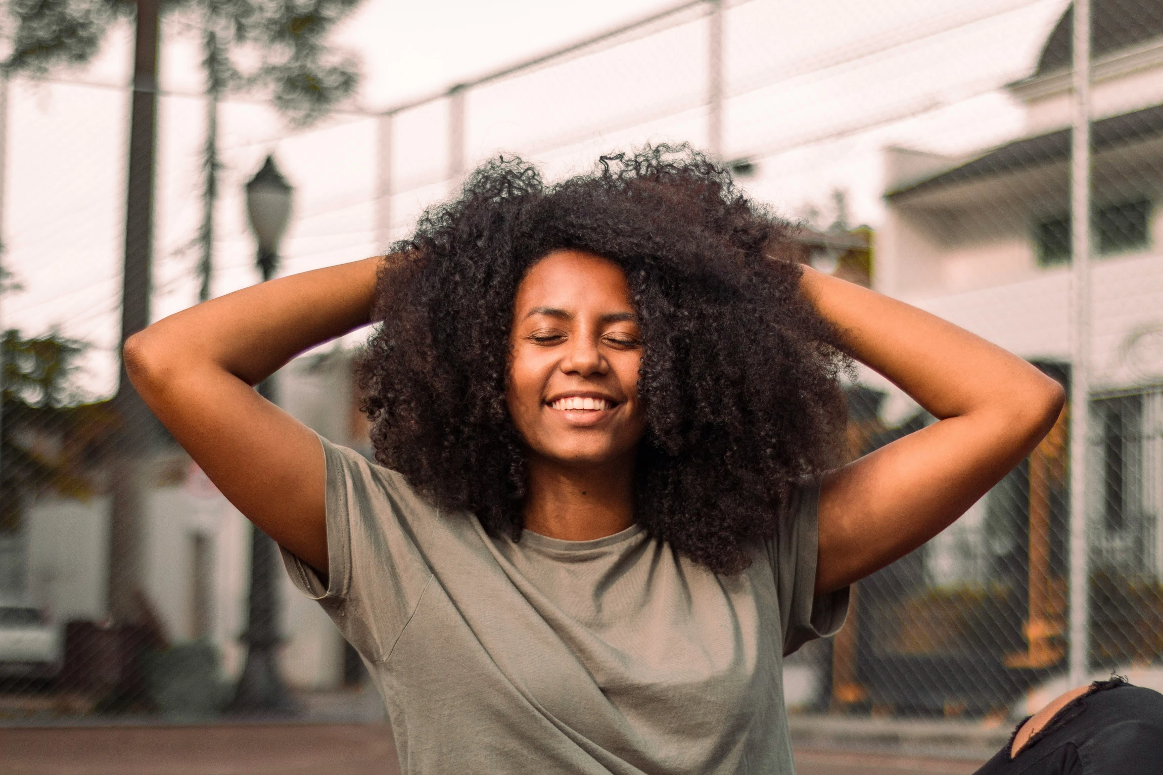 a woman with curly hair has her hands behind her head