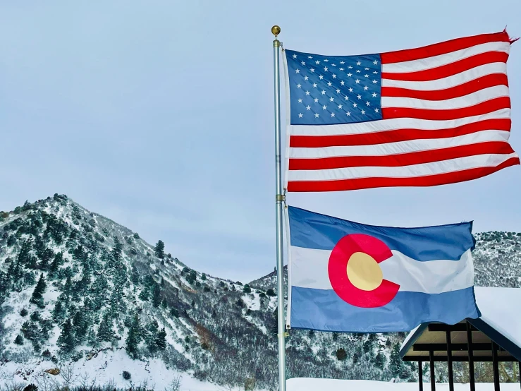 two american and colorado flags on a flagpole in the snow