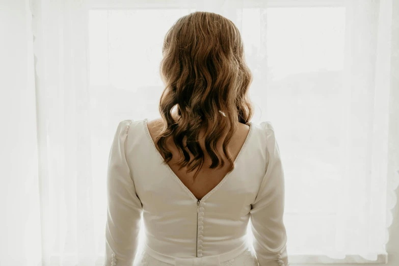 a woman in a white wedding gown is looking out the window