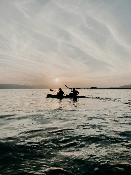 two people riding on kayaks in the water at sunset