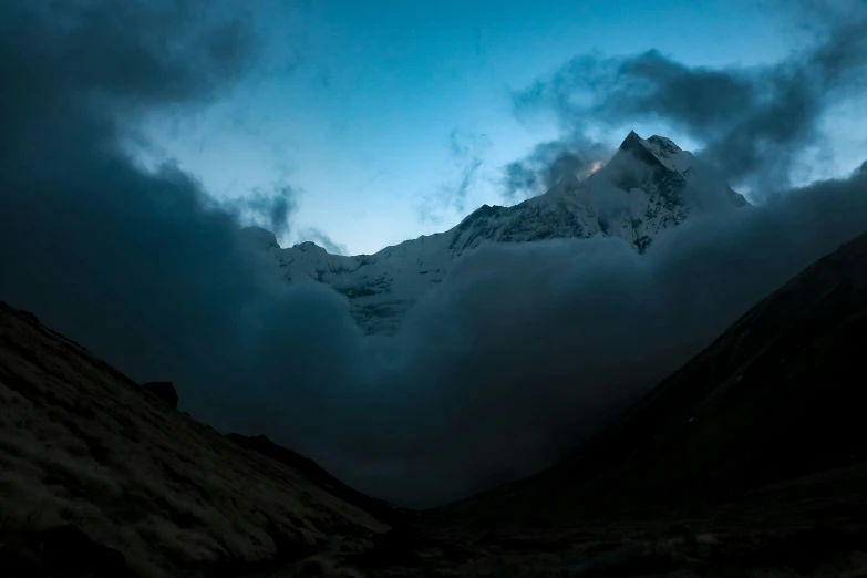 dark clouds hovering over a mountain, some below and the other side