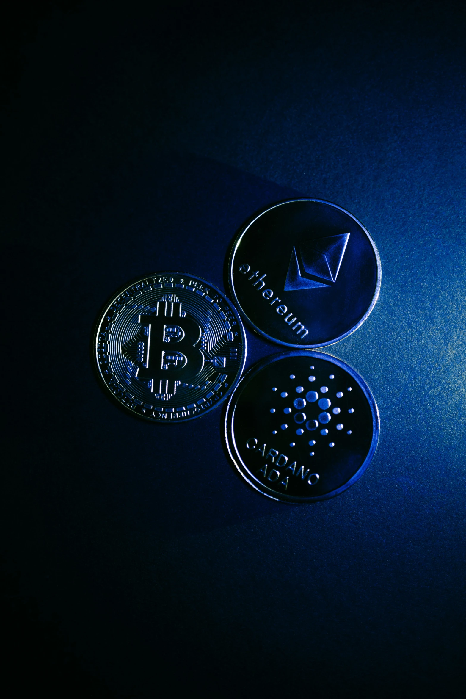 three shiny black bitcoins on a dark surface