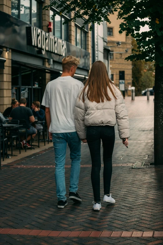 a couple walks down the sidewalk in front of a store