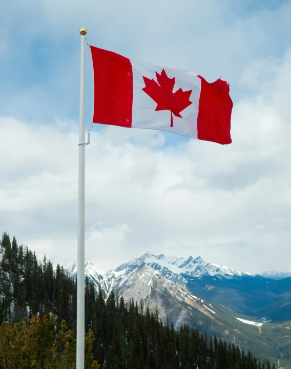 a canadian flag on top of a pole with mountains in the background