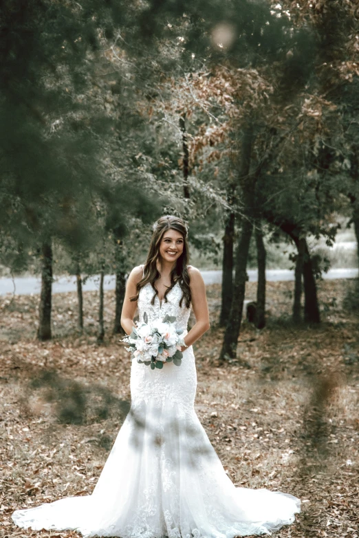 a bride stands in the woods and smiles for her wedding po