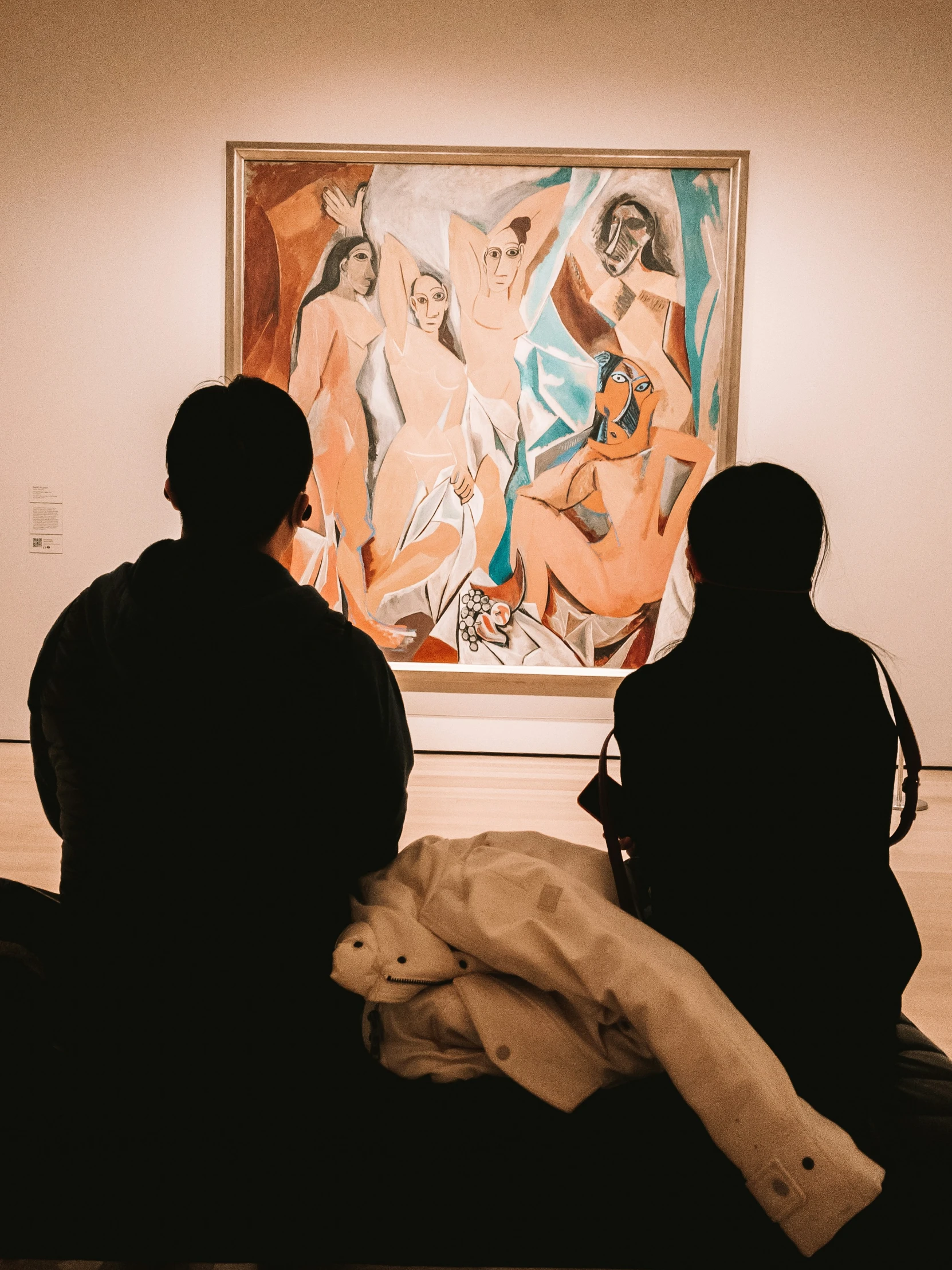 two people sitting in front of a painting in a museum