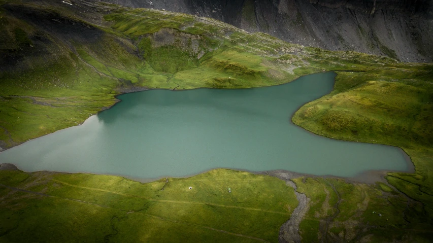 an overhead view of a lake and grassy hillside