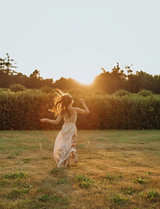 a girl is running in a field at sunset