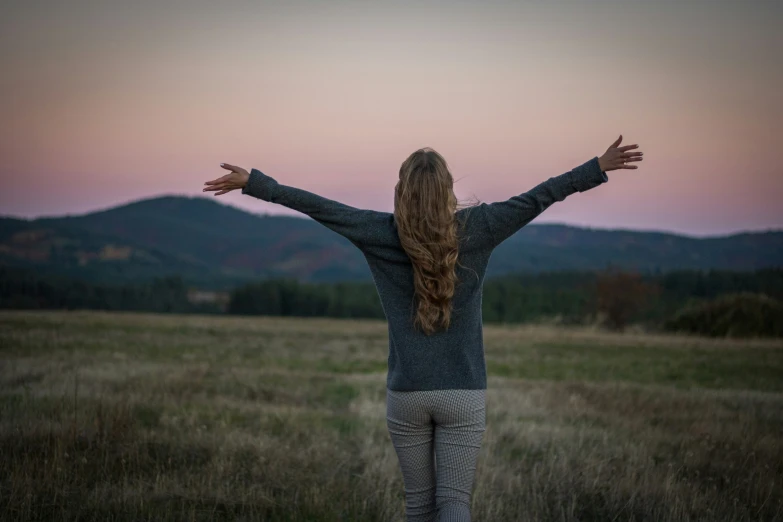 a woman is standing in a grassy field in the evening