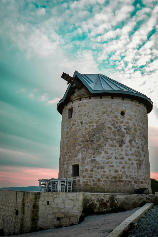 an old windmill on a beach with the sky and clouds in the background