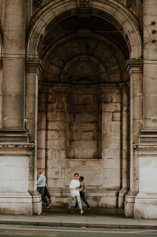 three people walk in front of an open stone archway