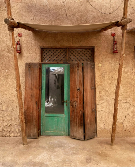 a green door and wooden poles next to a wall