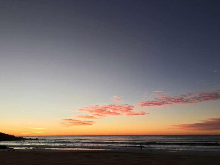 a person stands at the beach while the sun sets