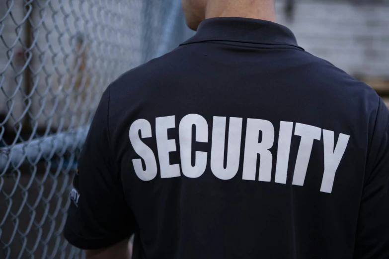 security man in black shirt standing by chain link fence