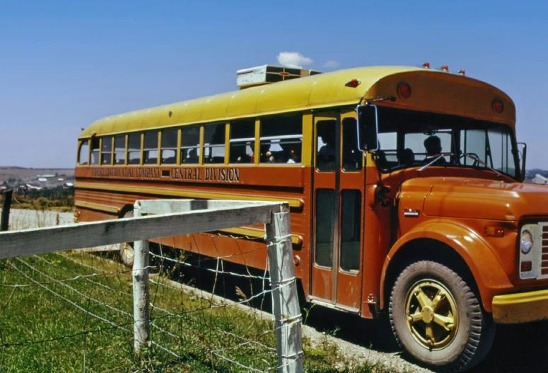 an old school bus sits parked by the fence