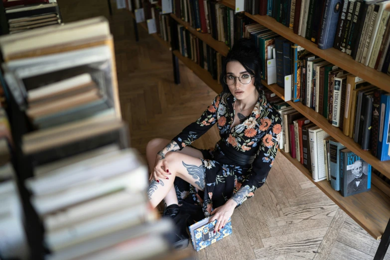 a lady sitting on the floor next to a large bookcase