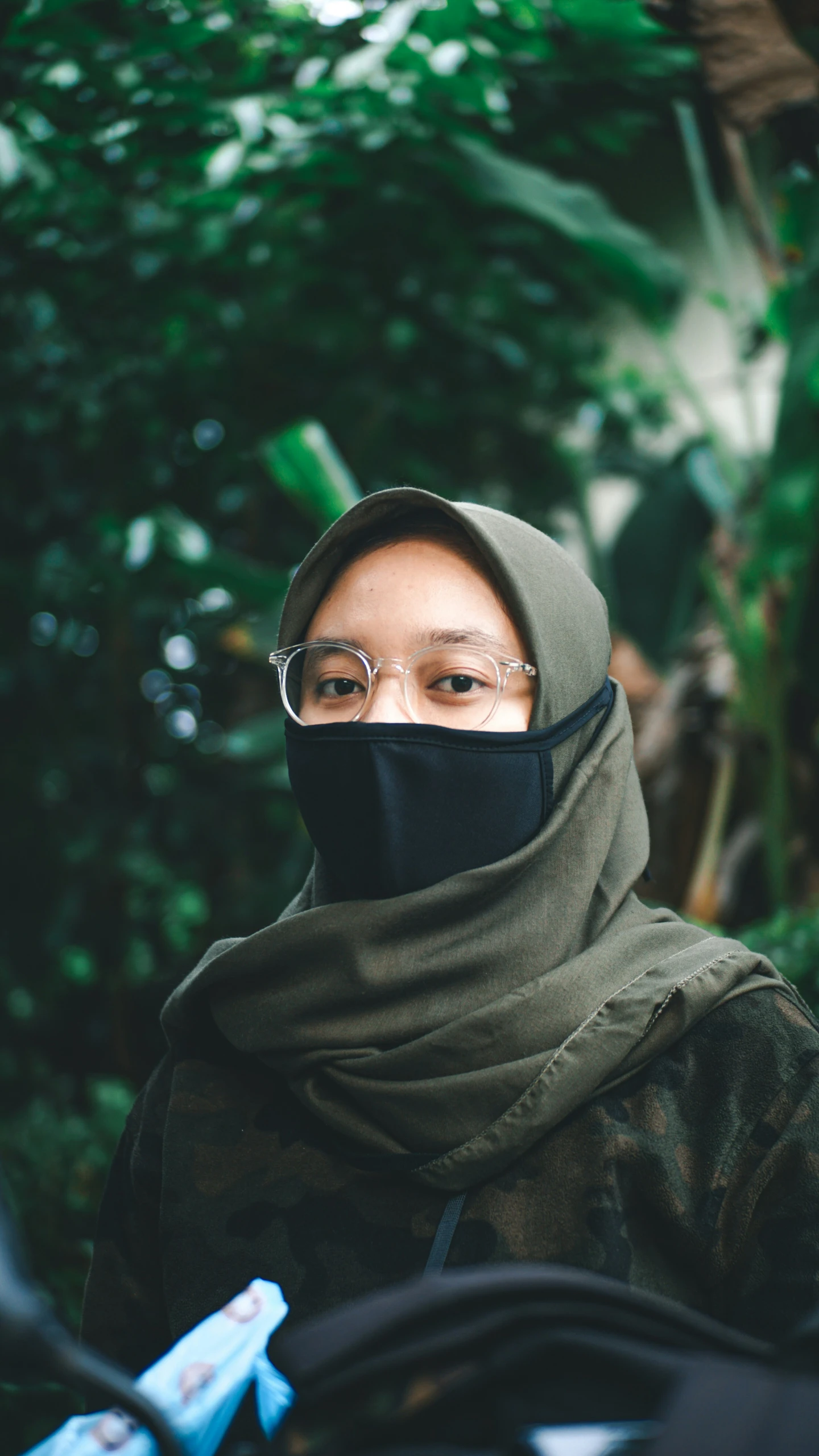 woman wearing head covering and glasses stands next to her motorcycle