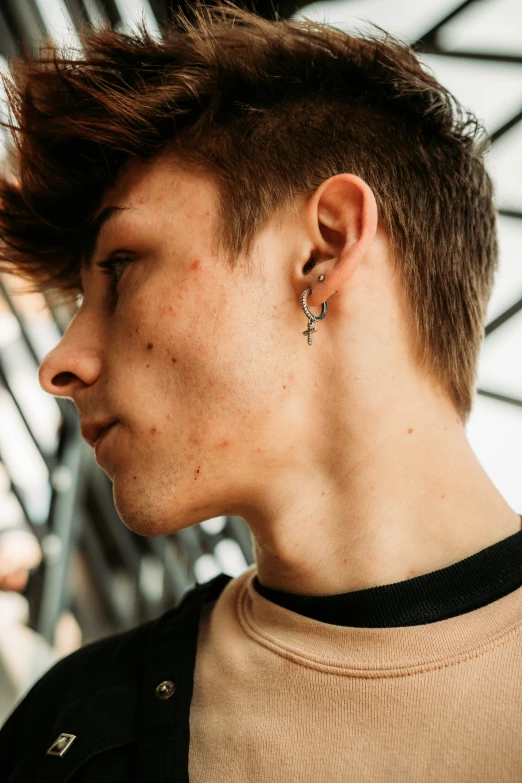 a young man in a brown shirt and black shirt with a piercing on his ear