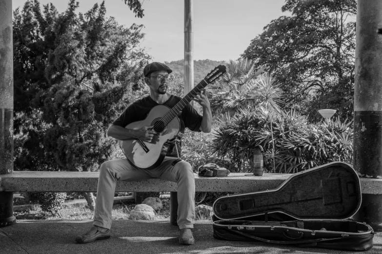 man sitting on park bench playing guitar outdoors