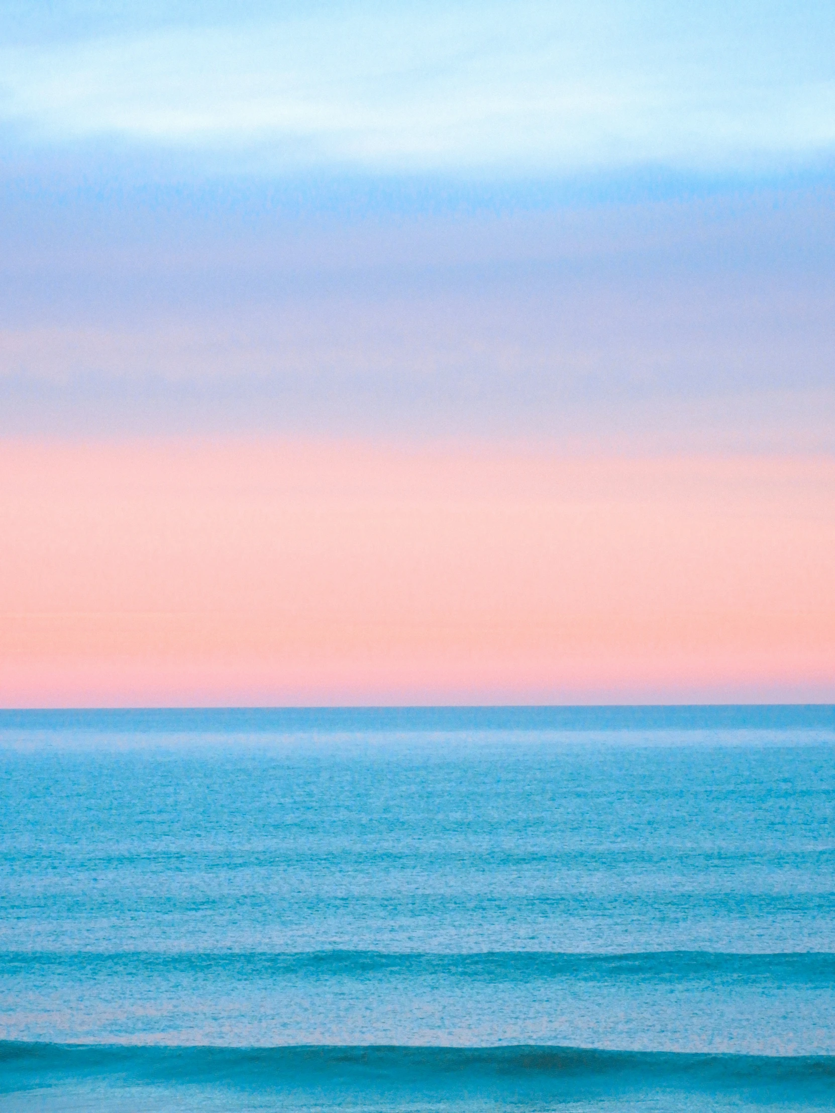 the ocean is blue, pink, and purple on the horizon