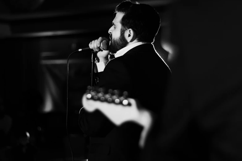 man in suit holding a guitar and singing into a microphone