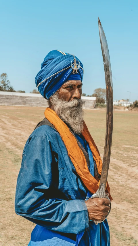 a man with a long beard wearing an blue outfit holds a large long knife