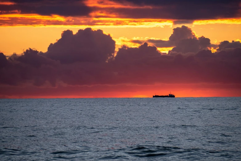 the sun sets over the ocean with a boat out in the distance