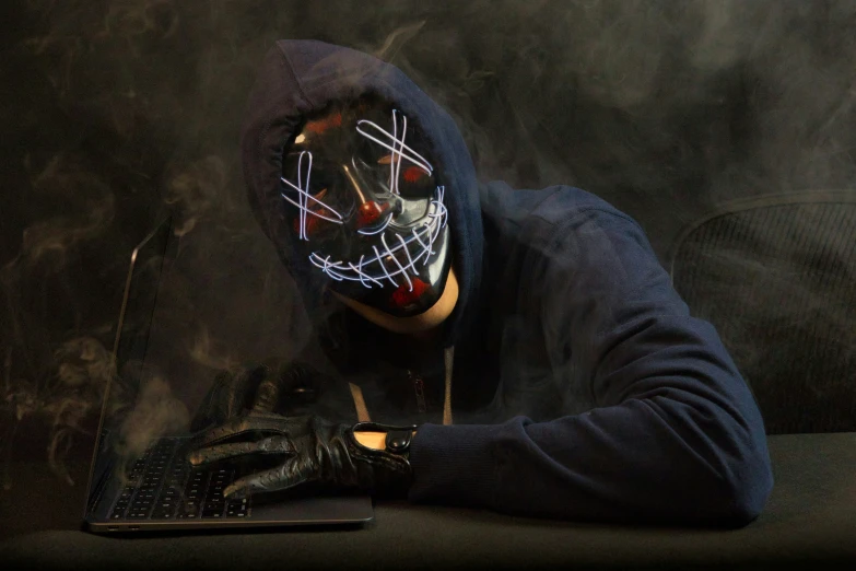 the person in the mask is sitting at his laptop