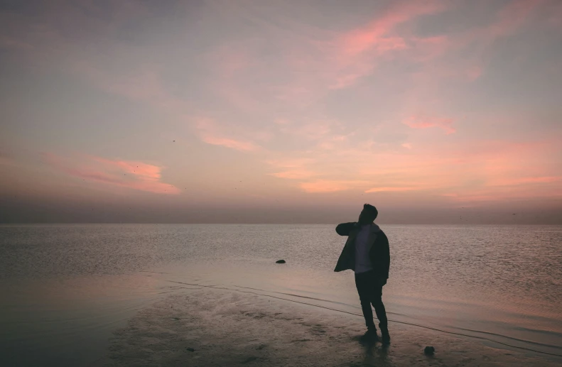 a person standing in the sand with their hands to their chest looking out into the water