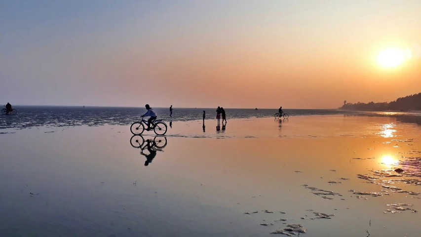 people riding bikes along the water's edge with a bright sun in the background