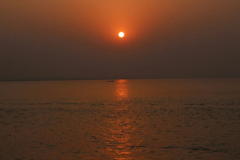 the setting sun shining in the middle of a body of water