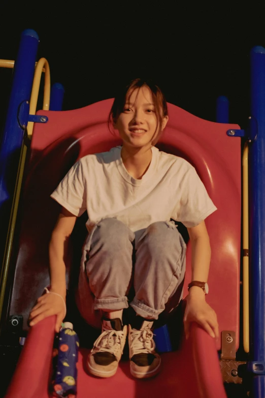 a girl with brown hair wearing white shirt and jeans sitting on a slide at the park