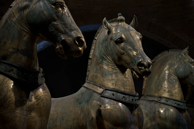 two bronzed statues depicting horses are against a black background