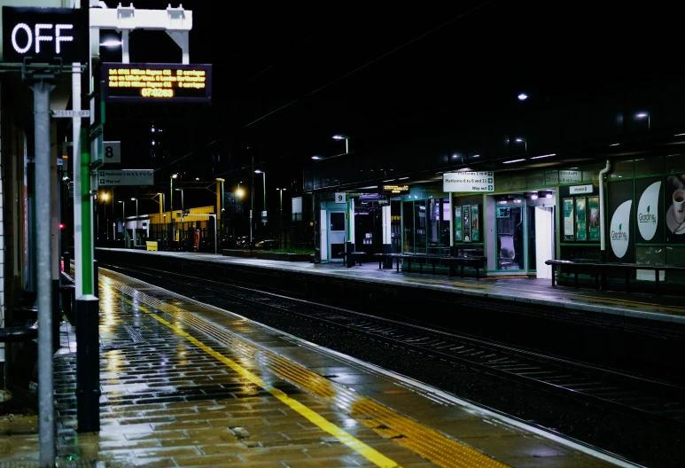 the train station has one empty platform, and the rest of the track is wet