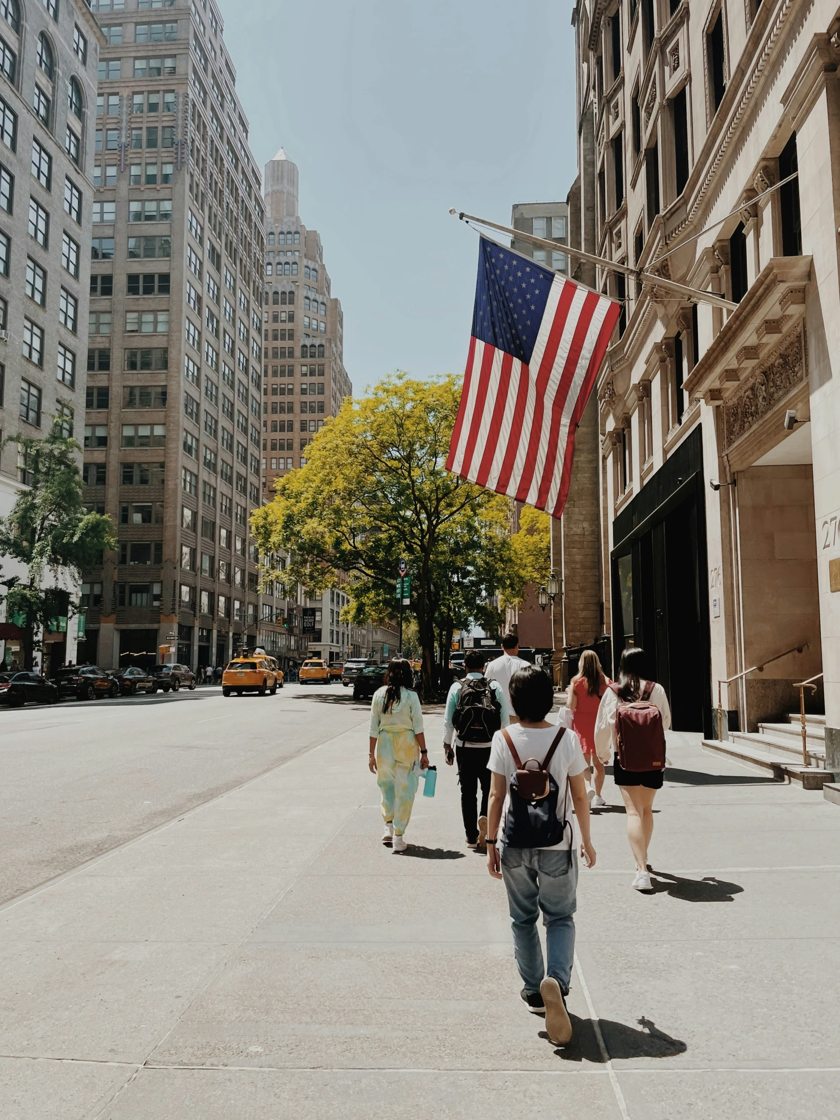 people walking down a street carrying backpacks and an american flag