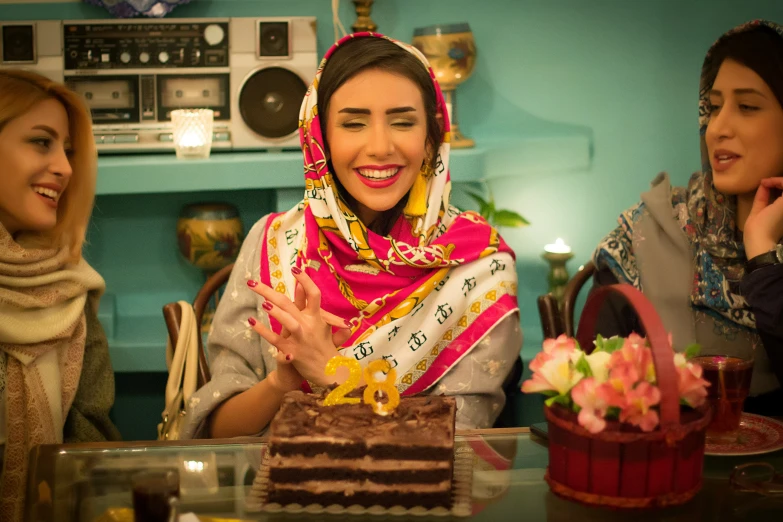 three women sitting around a table with a chocolate cake