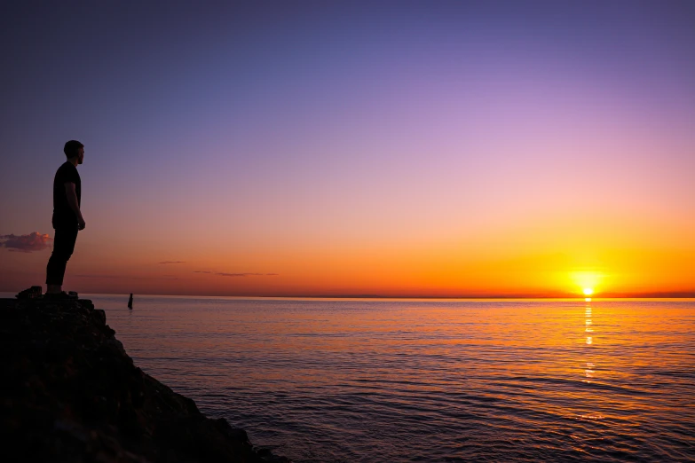 a person standing on a rocky cliff watching the sun go down over water