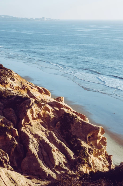 view over the edge of a hill in front of the ocean with a sandy shore