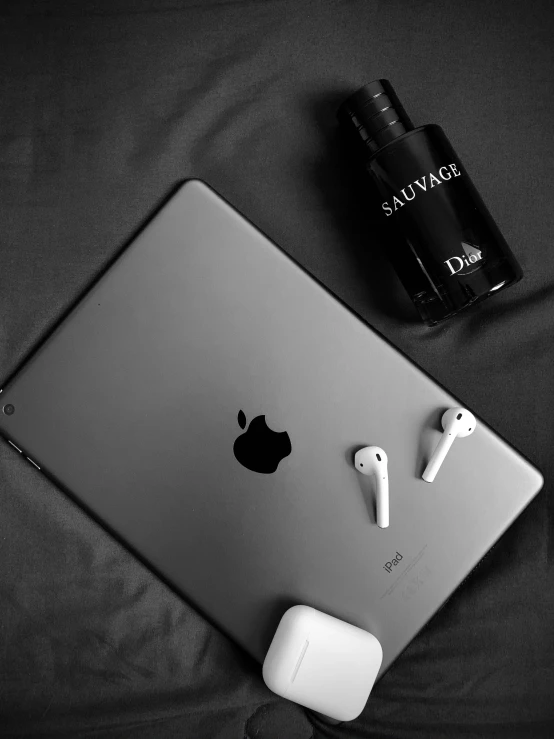 an apple tablet and earbuds sitting next to a bottle of gin