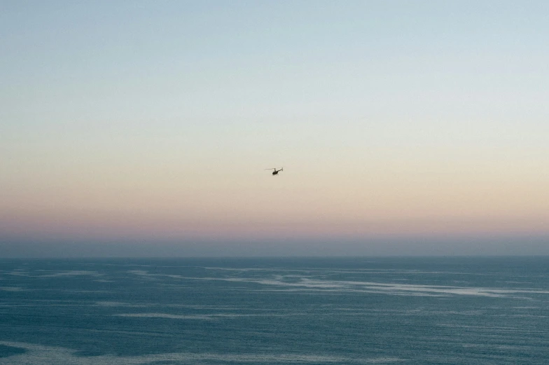 a bird flying over the ocean as the sun is setting