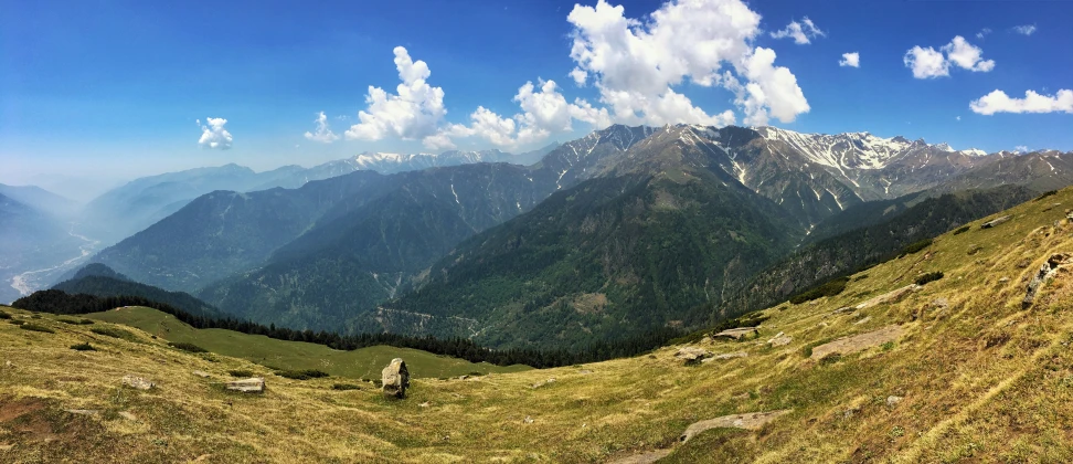 the top of a grassy mountain surrounded by large mountains