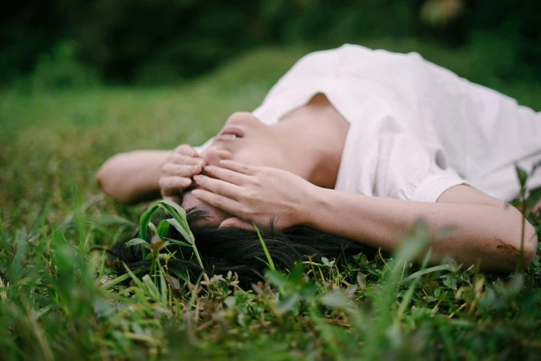 a girl lies on the grass and covers her eyes