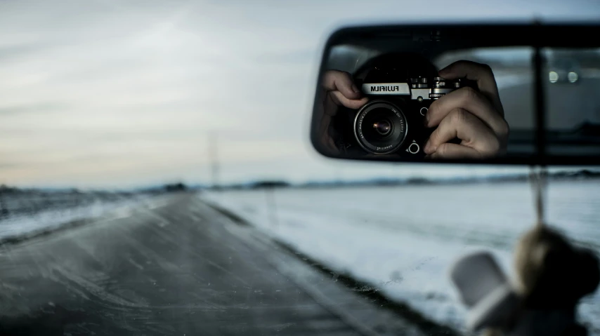 a rear view mirror showing the reflection of a person holding a camera