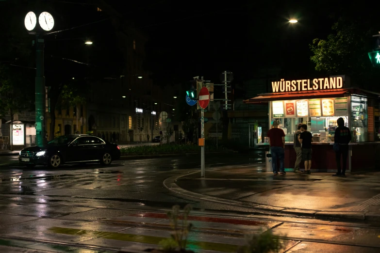 people stand at the corner outside a stand that has a sign with words