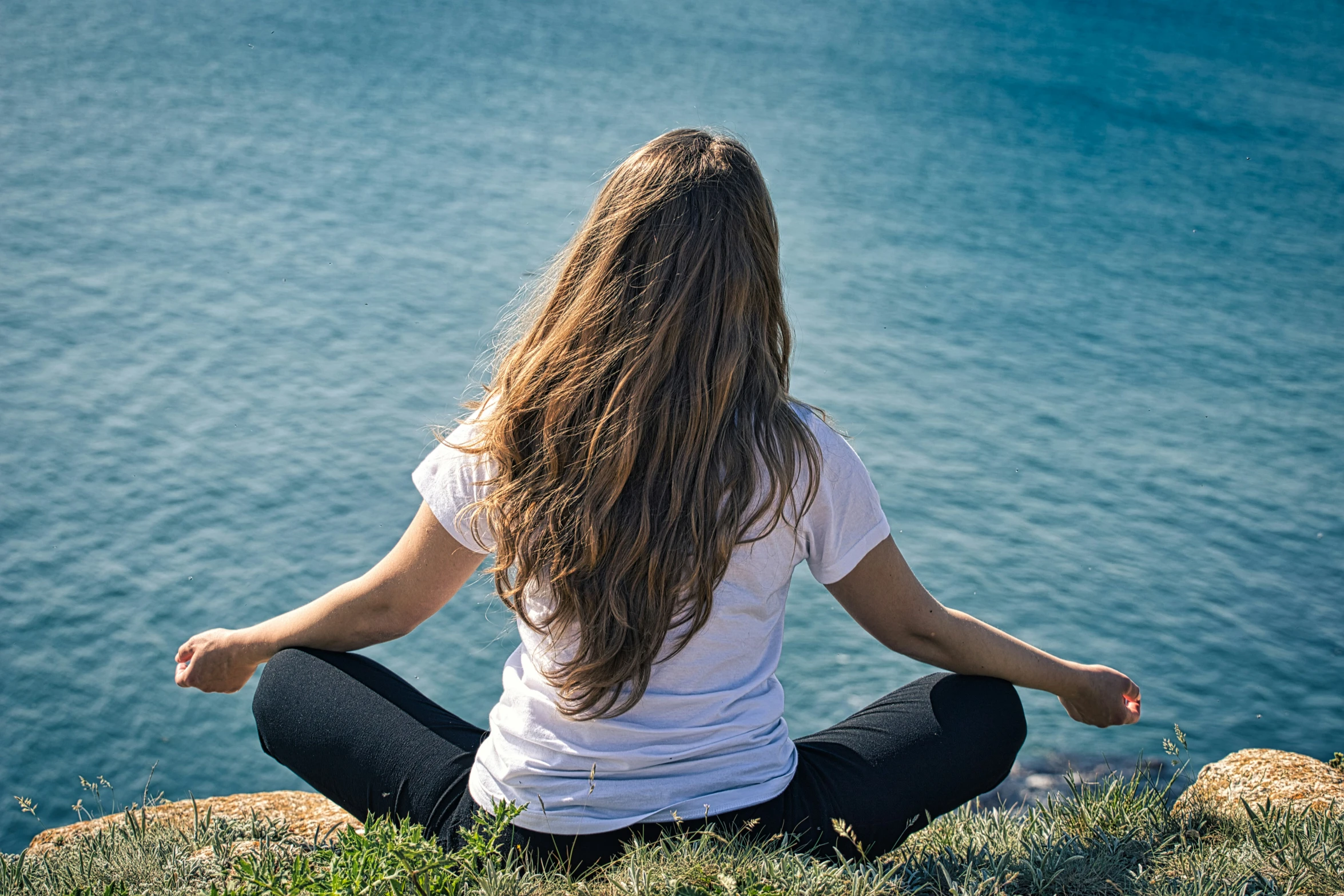 a woman is meditating near the ocean